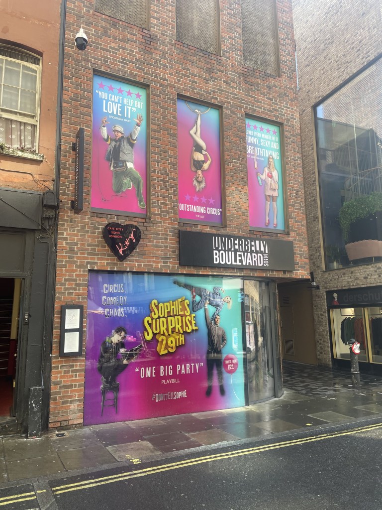 A window vinyl depicting a bright design advertising the show Sophie's Surprise 29th on the exterior of Underbelly Boulevard, a venue in Soho.